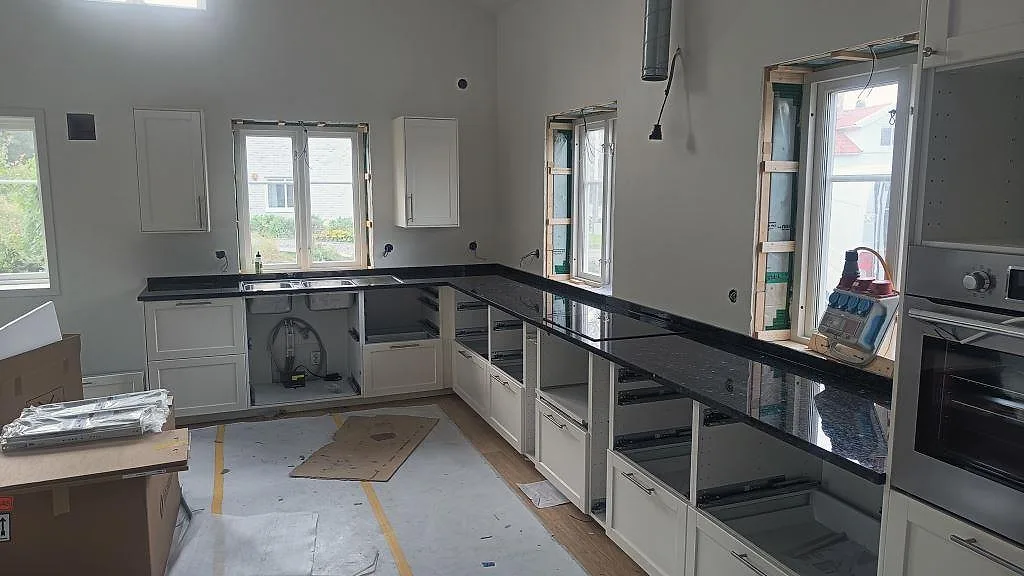 L-formad köksbänkskiva i polerad Emerald Pearl granit vid stora fönster i ett kök i Hönö.