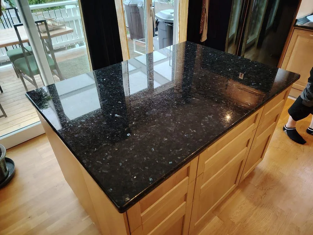 Köksö med bänkskiva i polerad Emerald Pearl granit på träinredning i ett kök i Huddinge.
