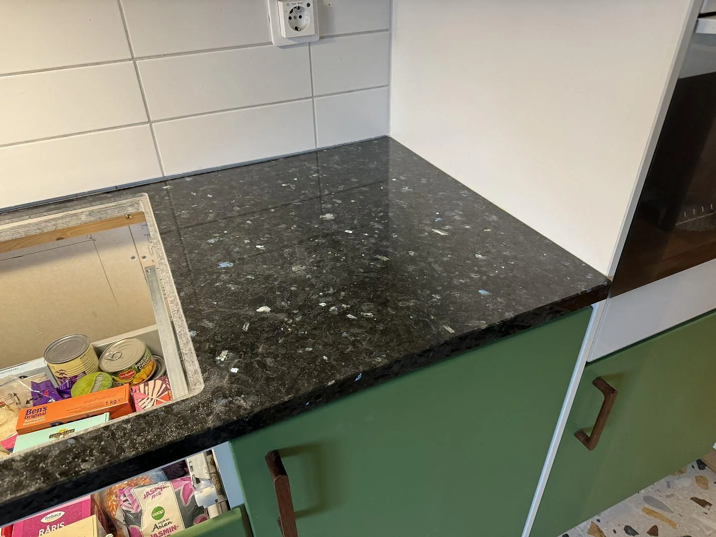 Installerad bänkskiva i Emerald Pearl granit, polerad, vid vit kakelvägg och gröna köksluckor i Lund.