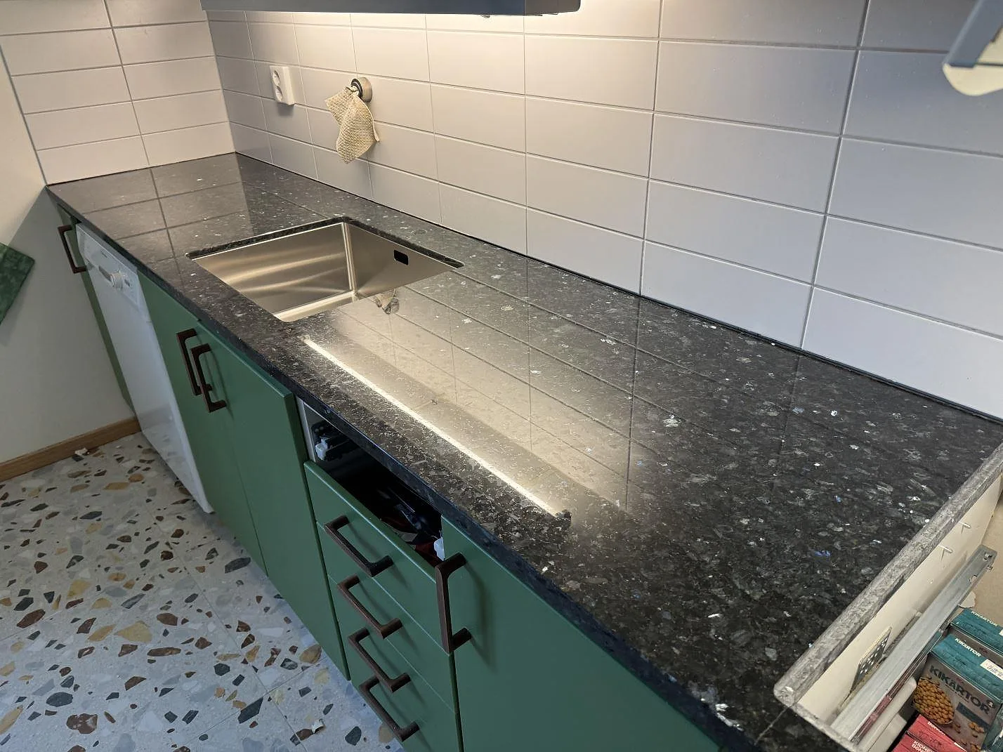 Köksbänkskiva i Emerald Pearl granit, polerad, med underlimmad rostfri diskho och gröna köksluckor i Lund.