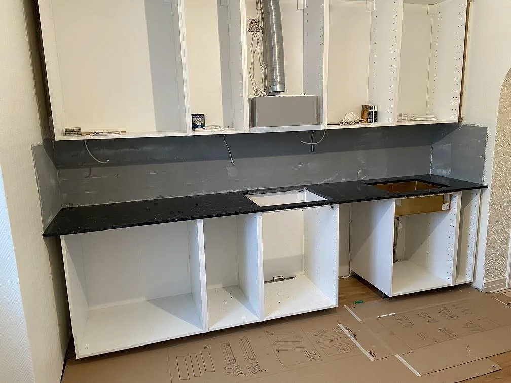Köksbänkskiva i mörk skimrande Emerald Pearl-granit, polerad, monterad längs en vägg med urtagning för diskho och häll i ett kök under montering i Malmö.