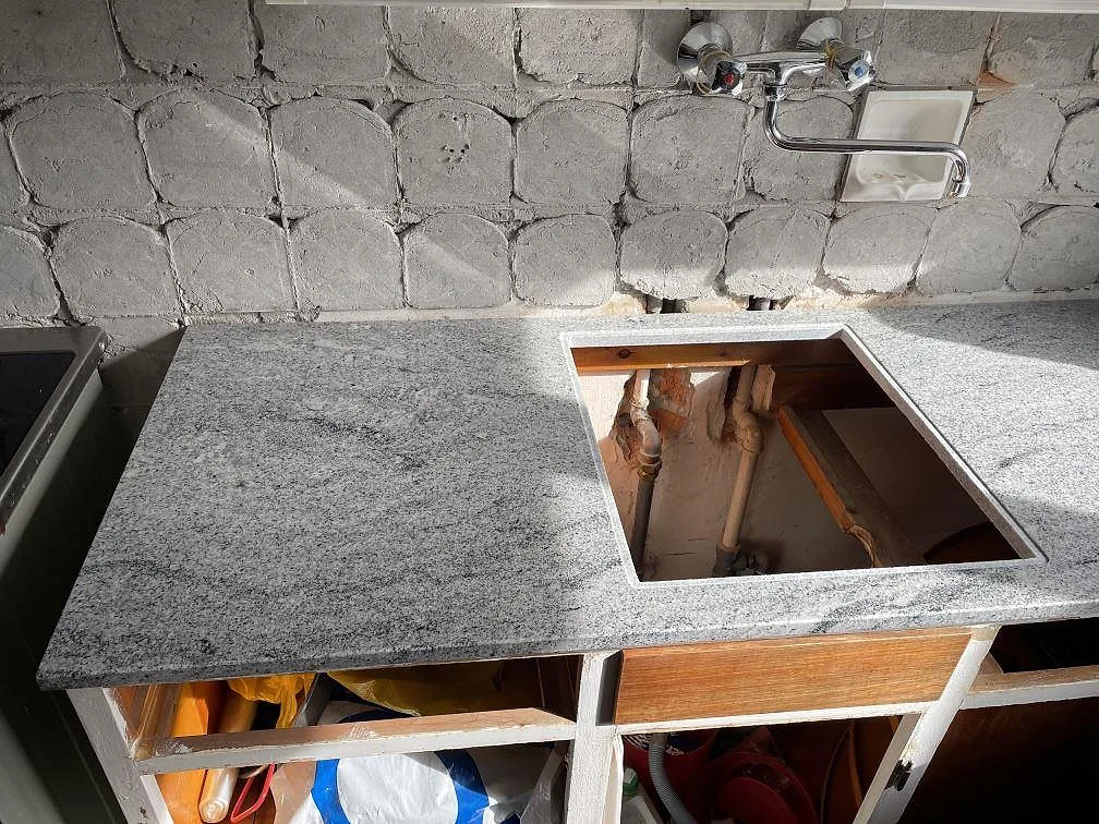 Köksbänkskiva i polerad Emerald Pearl granit med diskbänksurtag, blandare och öppna köksstommar i Ringsted.