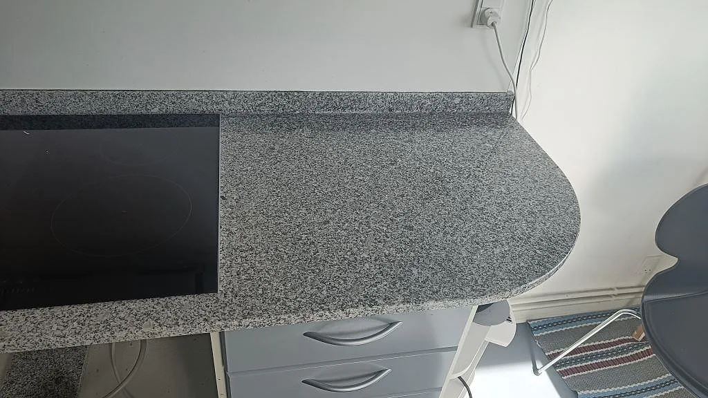Köksbänkskiva i grå granit Grigio Cristallo med mjukt rundad hörngavel och infälld induktionshäll i ett kök i Gentofte.