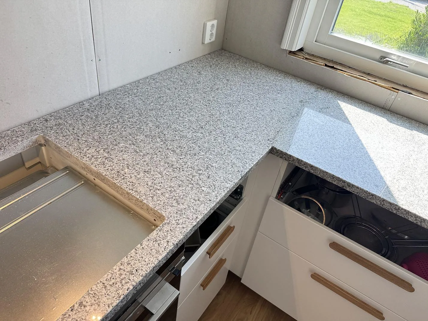 Köksbänkskiva i polerad Grigio Cristallo granit med L-formad arbetsyta och hällöppning i Hjärup.