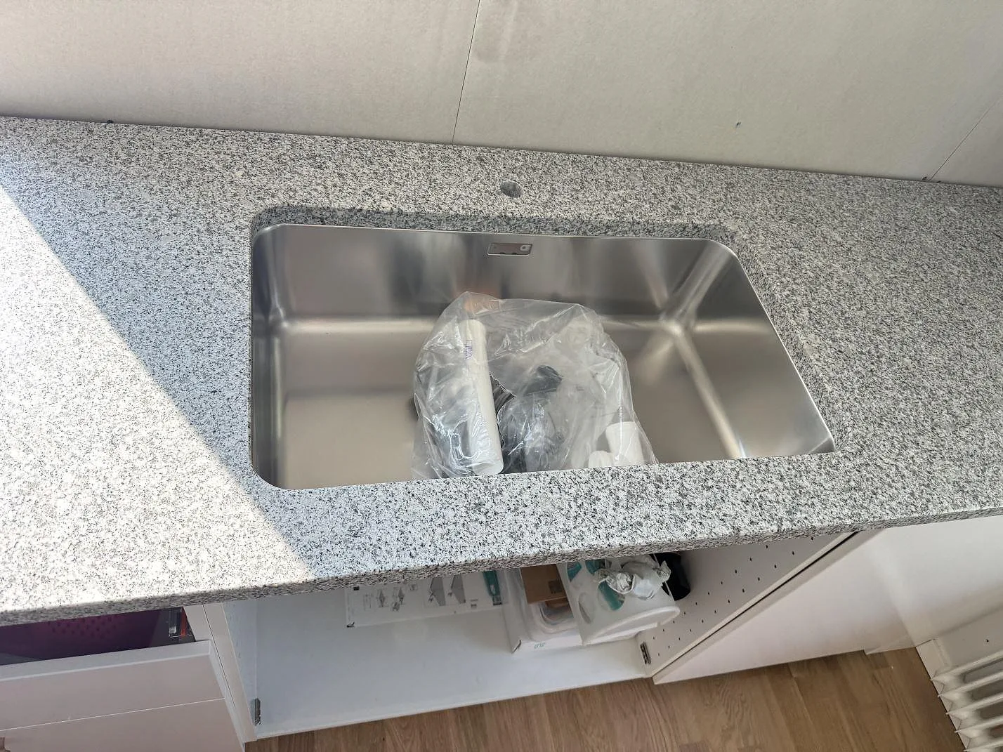 Närbild på rostfri diskho i polerad Grigio Cristallo granit med blandarhål i ett kök i Hjärup.