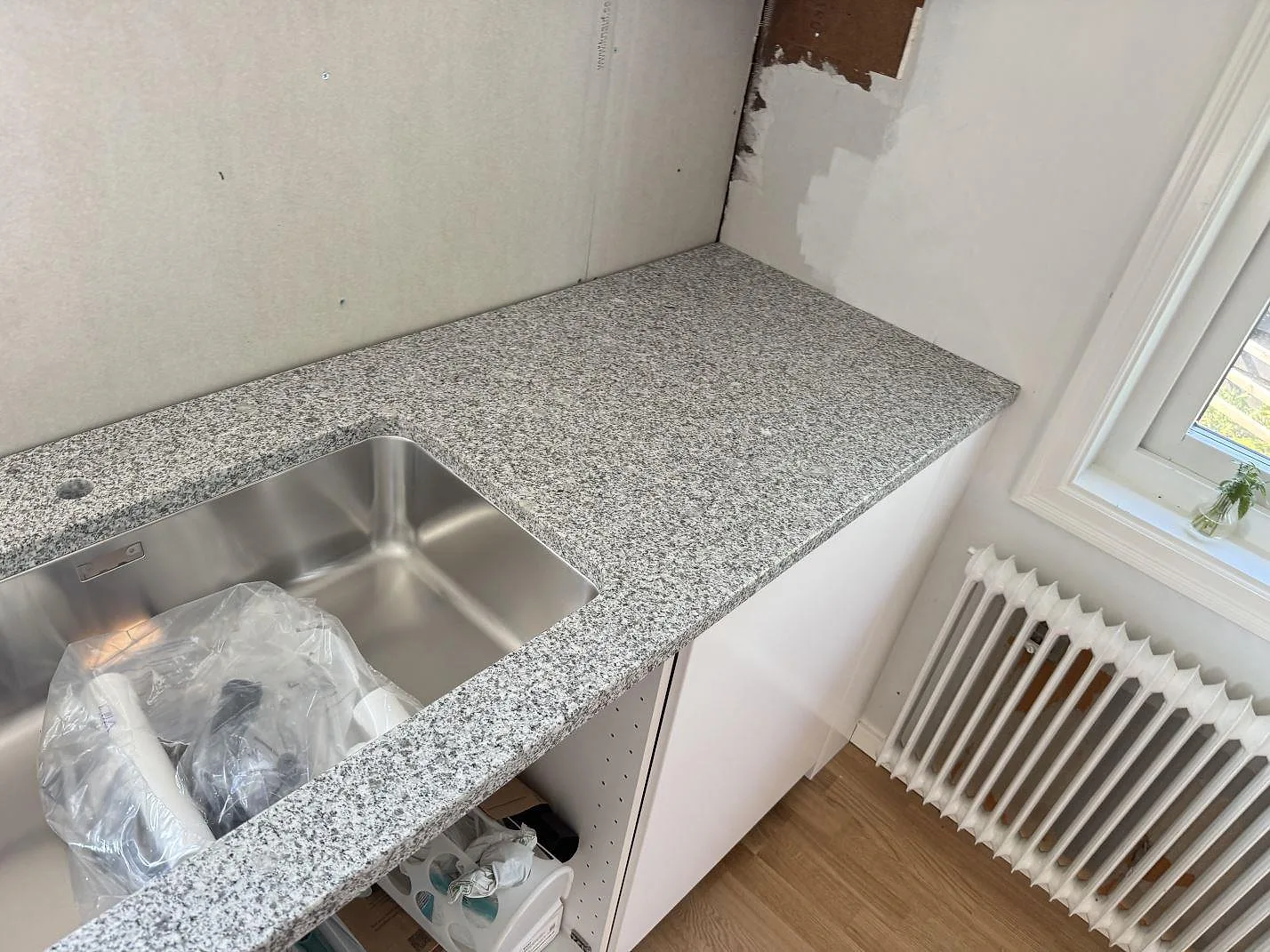 Polerad granitbänkskiva i Grigio Cristallo med rostfri diskho och arbetsyta vid fönster i kök i Hjärup.