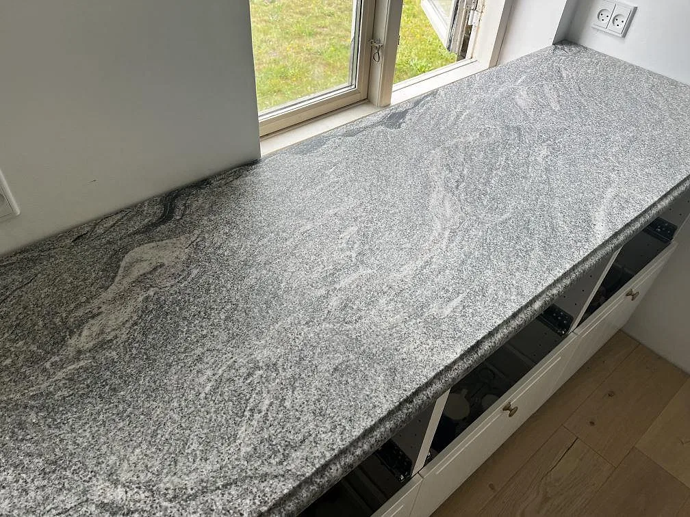 Närbild av polerad Grigio Cristallo granit som köksbänkskiva längs fönsterväggen i Kirke Hyllinge.