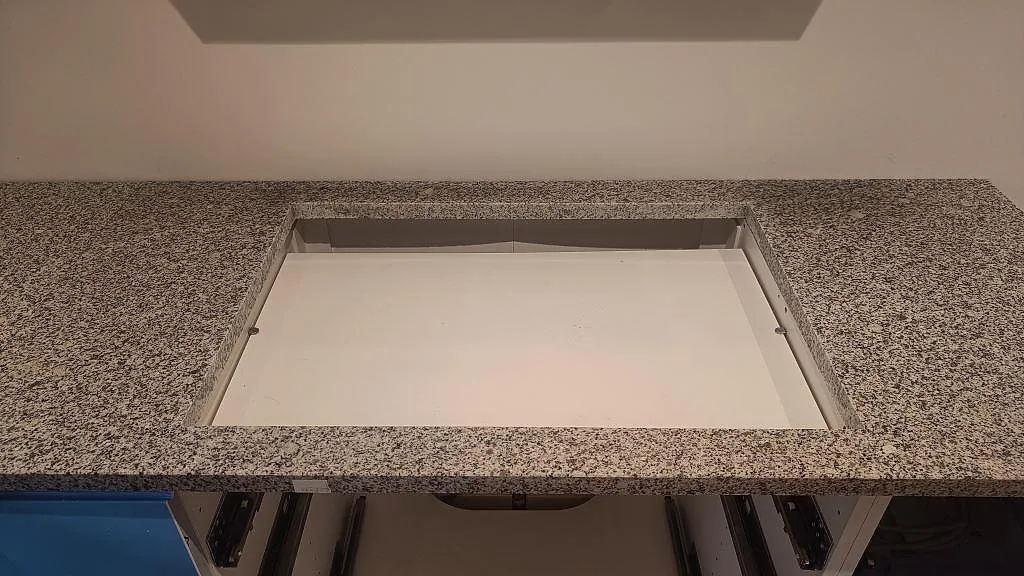 Hällöppning i polerad Grigio Cristallo granit ovanför blå köksstommar i ett kök i Laholm.
