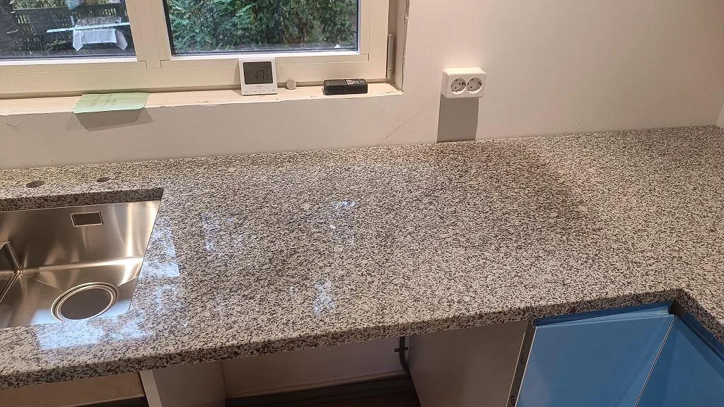 Polerad Grigio Cristallo granit med rostfri underlimmad diskho och arbetsyta under ett köksfönster i Laholm.