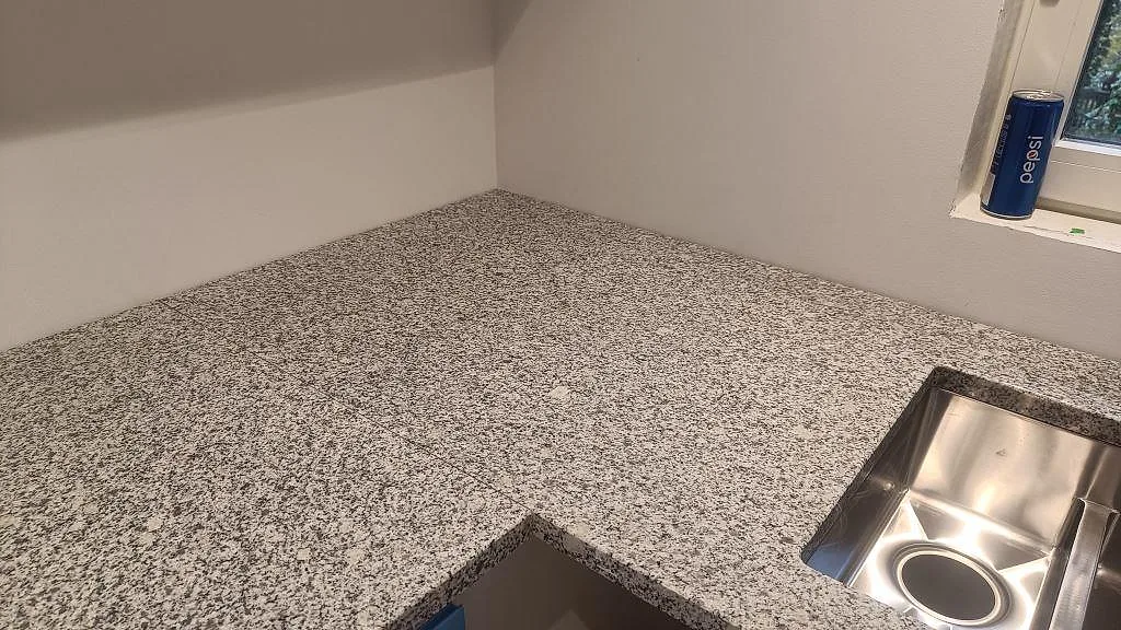 Närbild på hörn och diskzon i polerad Grigio Cristallo granit med rostfri diskho i Laholm.