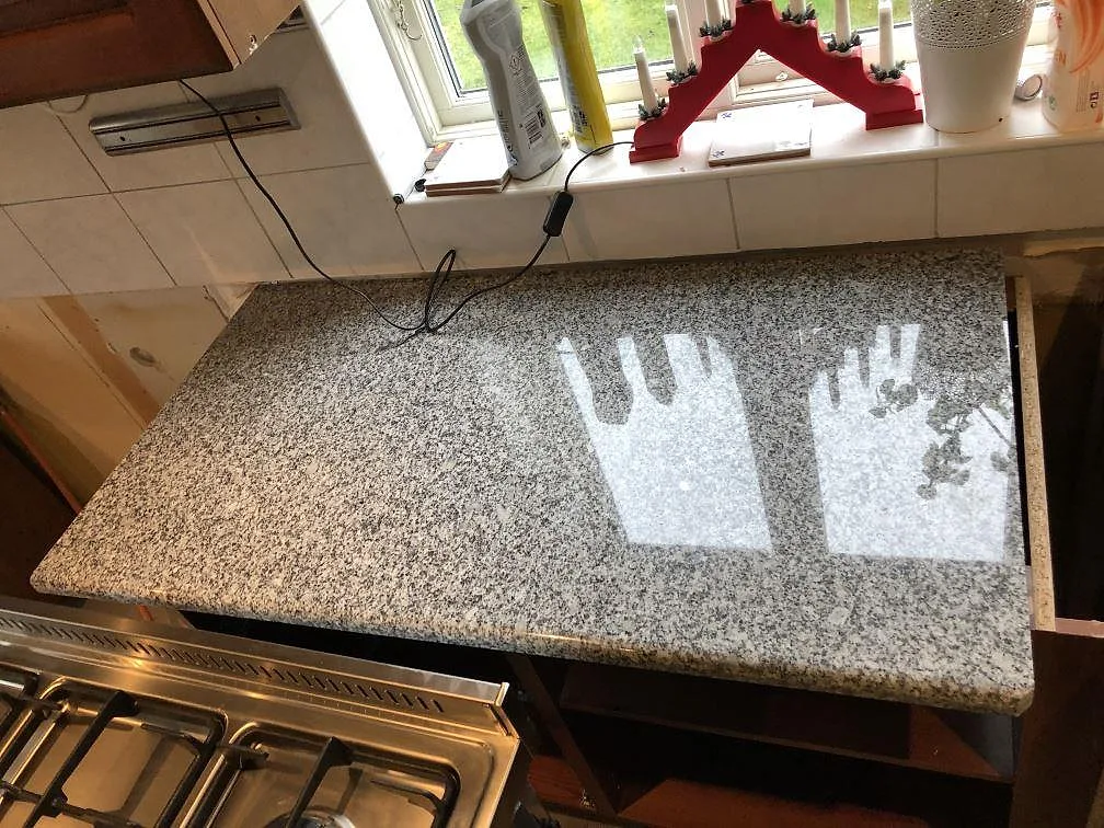 Köksbänkskiva i grått granit Grigio Cristallo, polerad, med rundad halvö och plats för underlimmad diskho i ett kök under montering i Onsala.