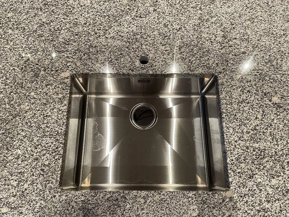 Detalj av underlimmad rostfri diskho i polerad Grigio Cristallo granit med blandarhål i ett kök i Simrishamn.
