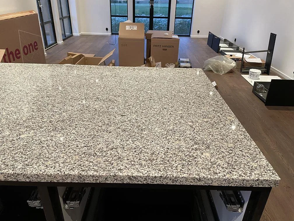 Närbild på polerad köksö i Grigio Cristallo granit under montering i ett kök med svart inredning i Simrishamn.