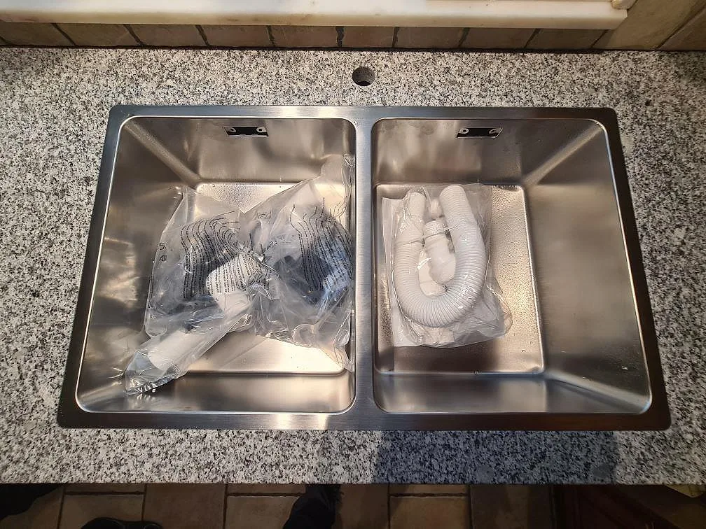 Dubbel rostfri diskho i en polerad Grigio Cristallo bänkskiva med blandarhål vid kaklat fönster i Spånga.
