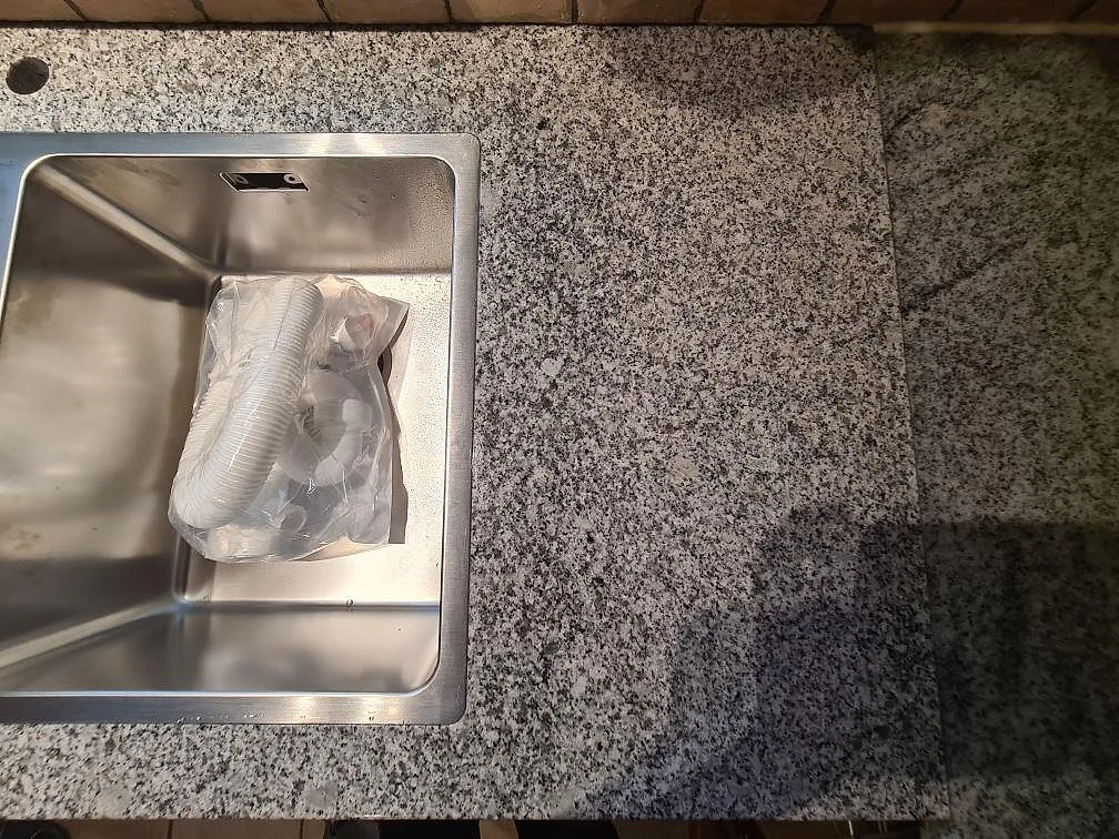 Detalj av polerad Grigio Cristallo granit bredvid rostfri diskho och blandarhål under montering i Spånga.