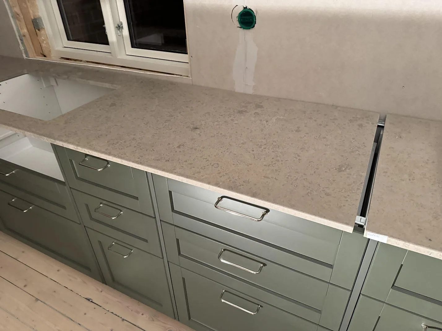 Jura Grey kalksten som matt köksbänkskiva under fönster med gröna köksluckor i Älmhult.