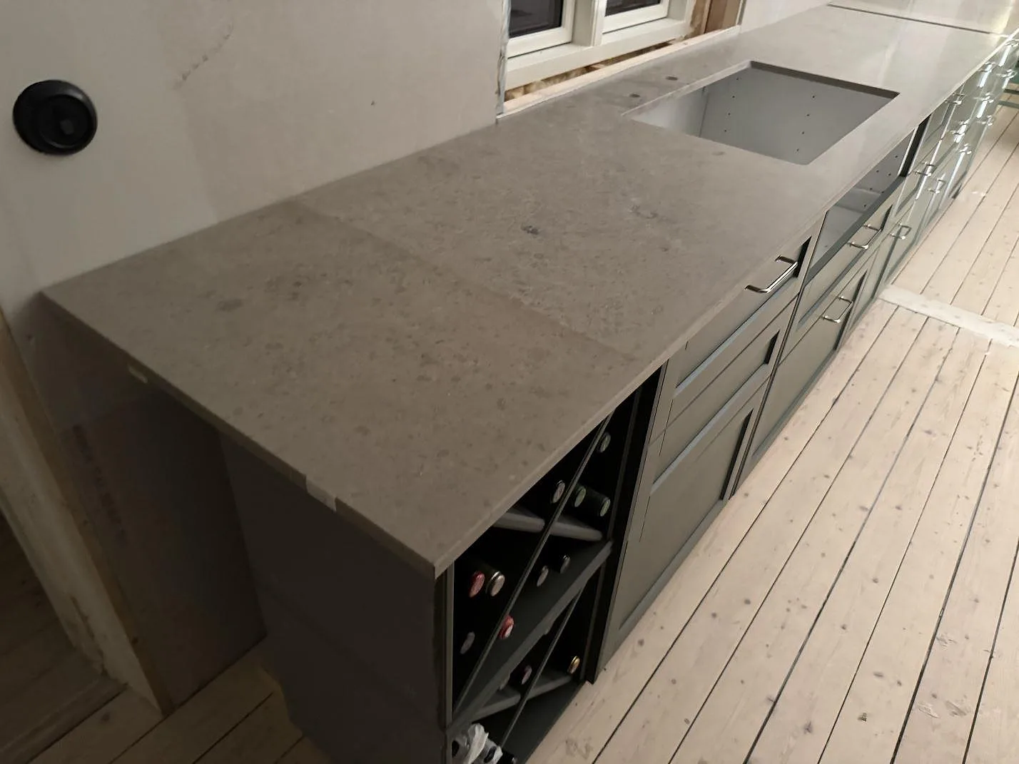 Lång köksbänkskiva i matt Jura Grey kalksten med vasköppning och gröna luckor i Älmhult.