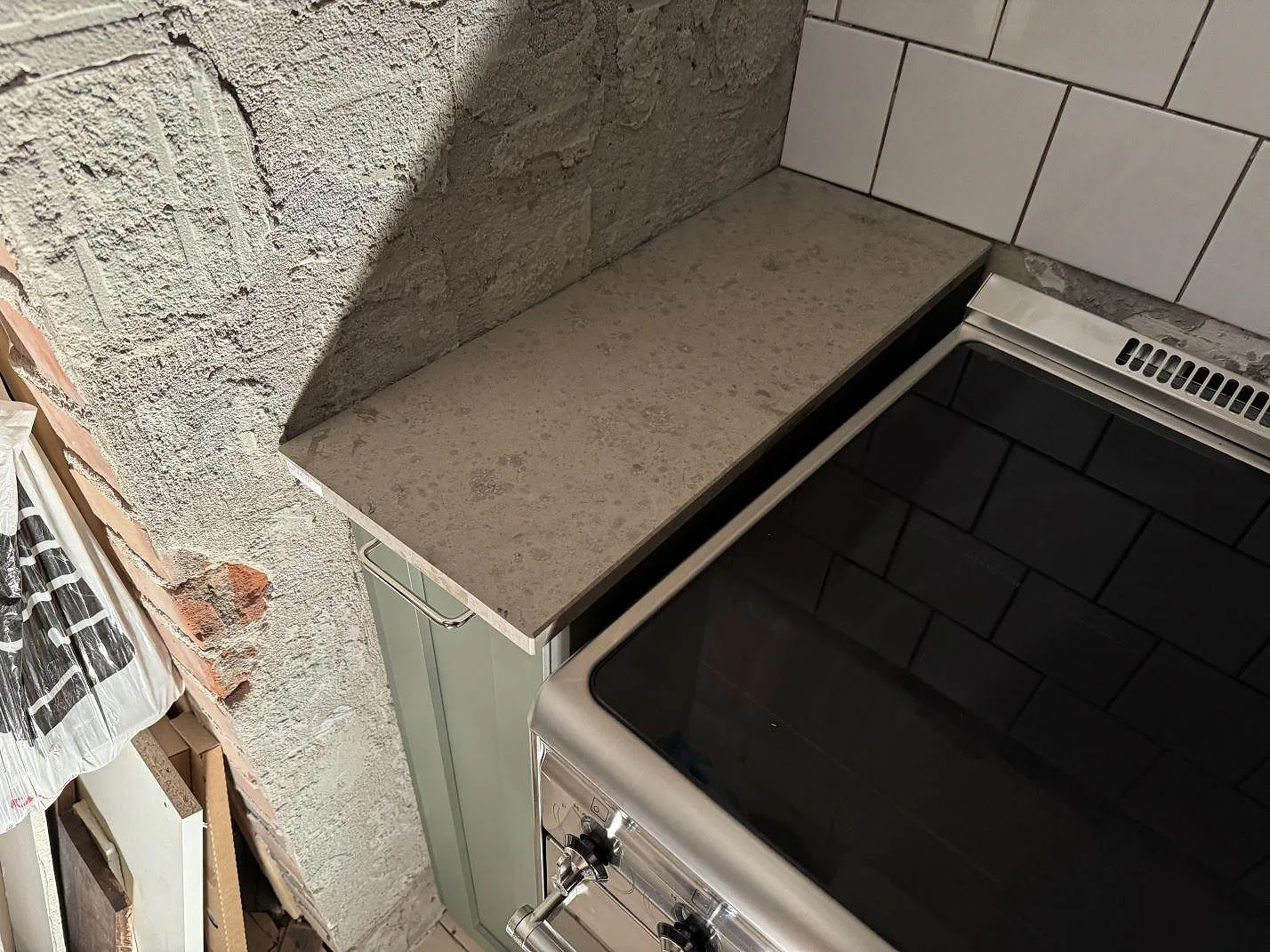 Kort bänkskiva i matt Jura Grey kalksten bredvid spisen i ett kök under montering i Älmhult.