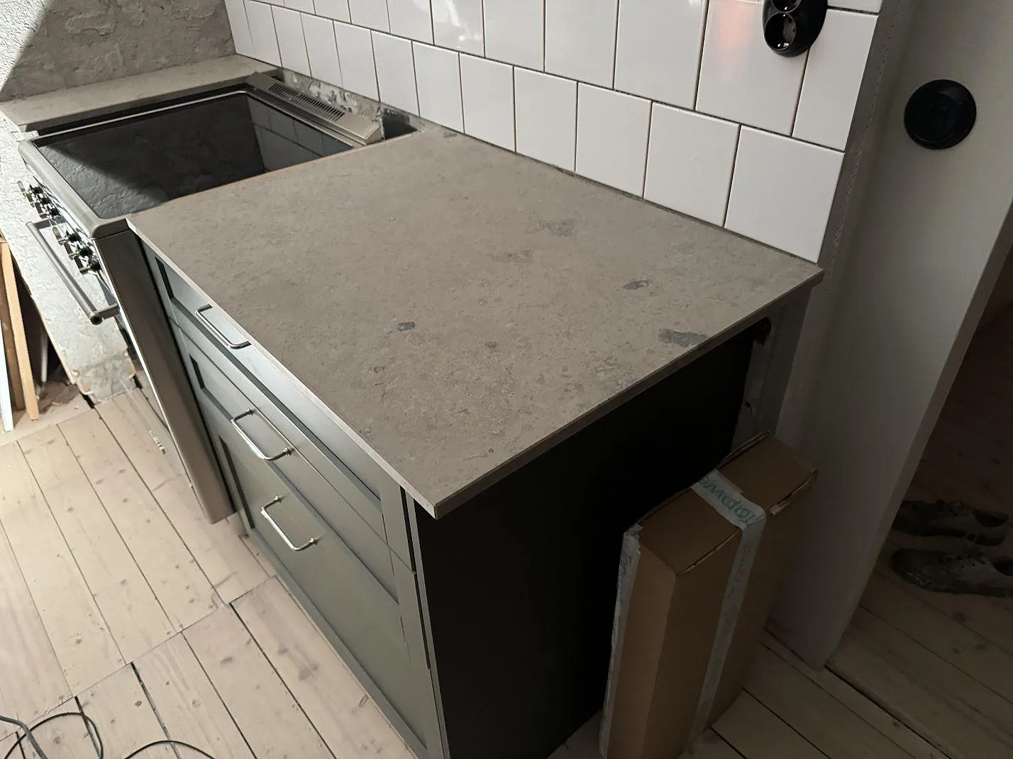 Köksbänkskiva i matt Jura Grey kalksten vid spis och vit subwaykakel i ett kök i Älmhult.