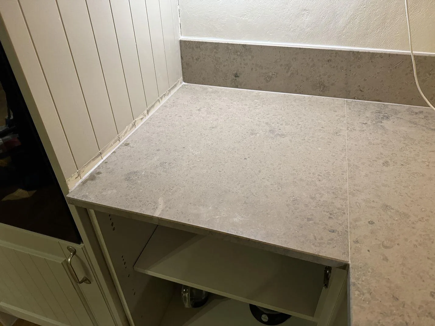 Detalj av matt Jura Grey kalkstensbänkskiva med stänkkant över vita köksstommar i Ängelholm.