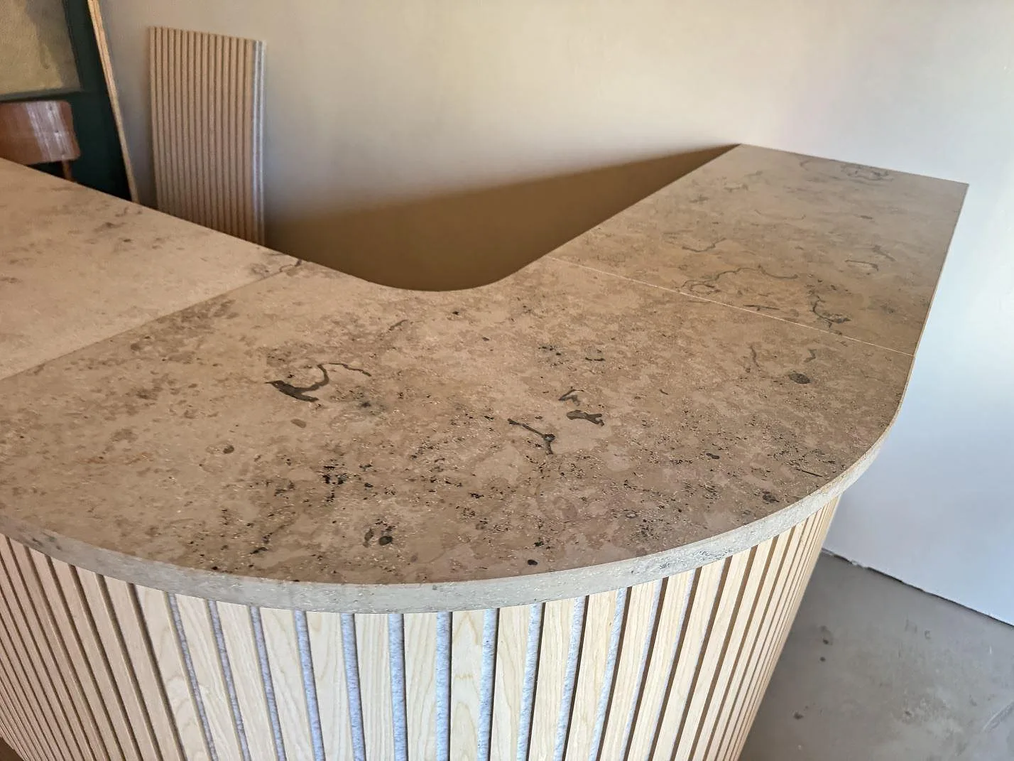 Svängd bänkskiva i matt Jura Grey kalksten på ribbad träbas i en receptionsmiljö i Anderslöv.