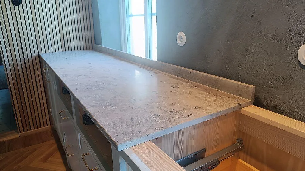 Köksbänkskiva i Jura Grey, matt kalksten, med låg stänkkant längs fönsterväggen i ett kök i Arlöv.