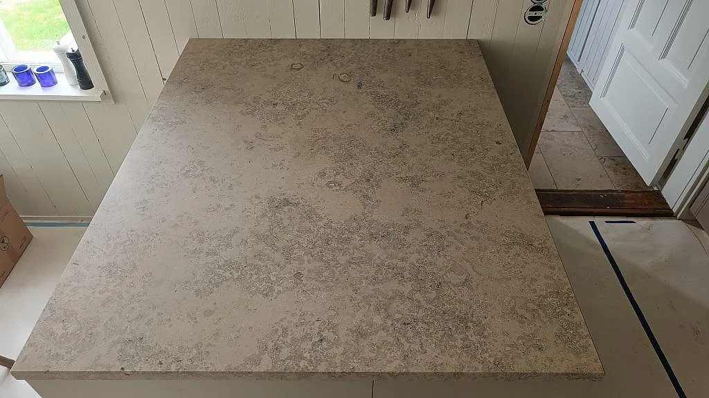 Stor köksö i Jura Grey kalksten ovanifrån, matt grågul yta med fossiler, vid fönster i ett kök i Båstad.