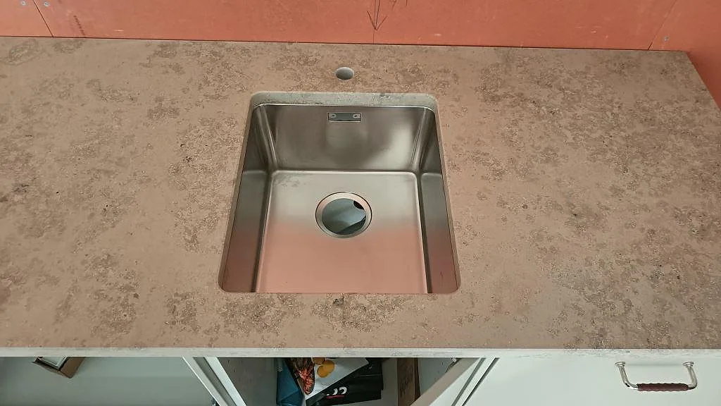 Underlimmad fyrkantig rostfri diskho i en köksbänkskiva av Jura Grey kalksten i Båstad, matt yta.