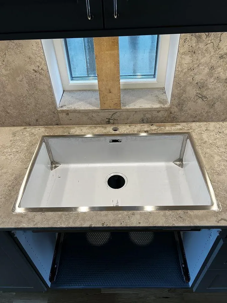 Detalj av diskhoöppning i köksbänkskiva av matt Jura Grey kalksten med fönster bakom i Bankeryd.
