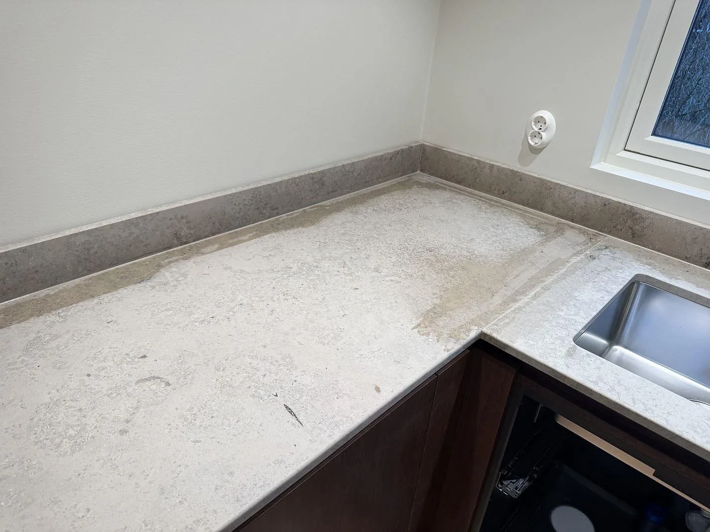 Matt köksbänkskiva i Jura Grey med gråbeige fossilstruktur, låg stänkkant och diskho under fönster i Borås.