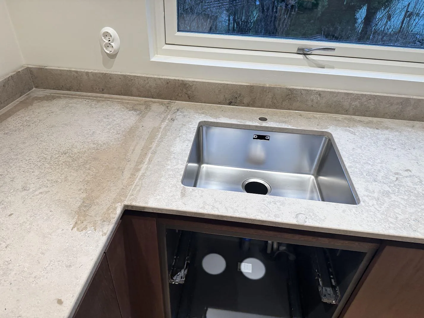 Underlimmad rostfri diskho i en köksbänkskiva av matt Jura Grey kalksten med stänkkant under fönster i Borås.