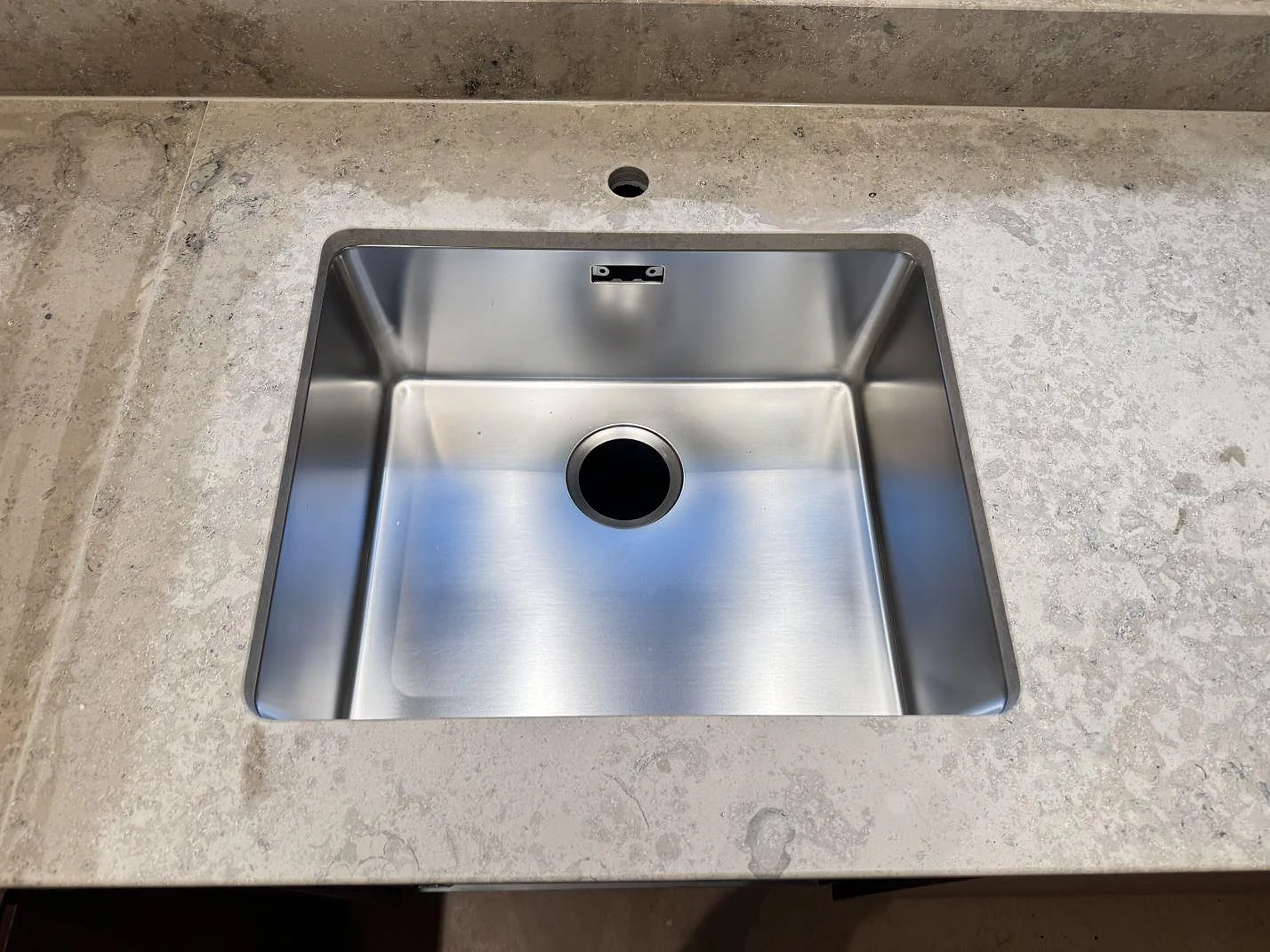 Detalj av rostfri diskho monterad under en matt Jura Grey bänkskiva med synlig fossilådring i Borås.