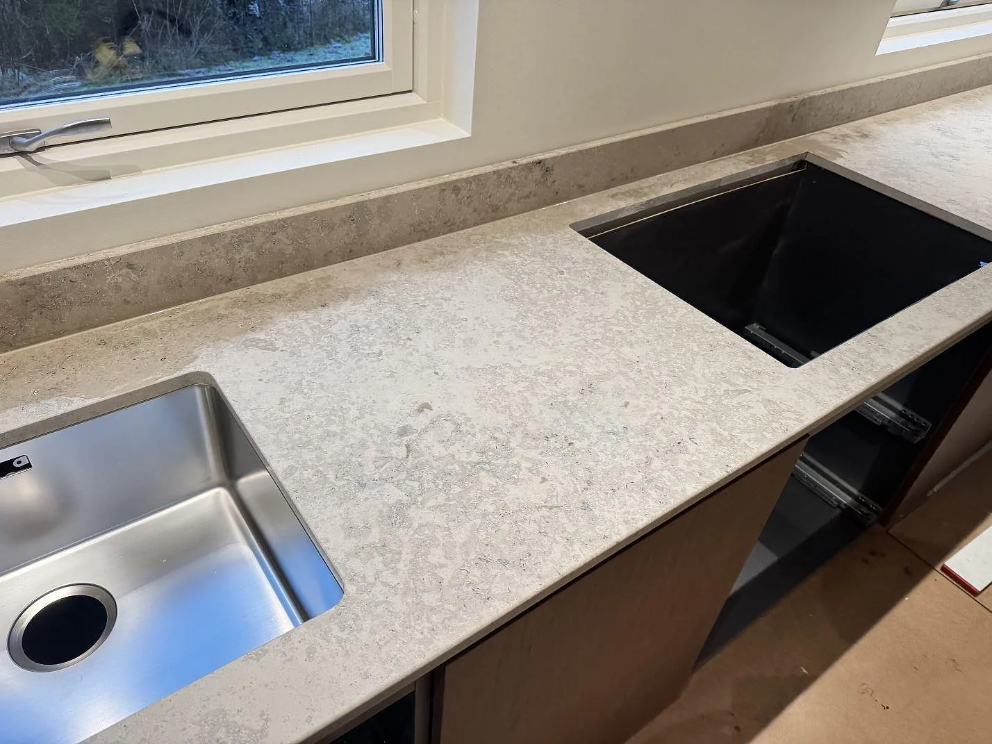 Köksbänkskiva i matt Jura Grey kalksten med rostfri diskho, öppen hällurtagning och låg stänkkant i ett kök i Borås.