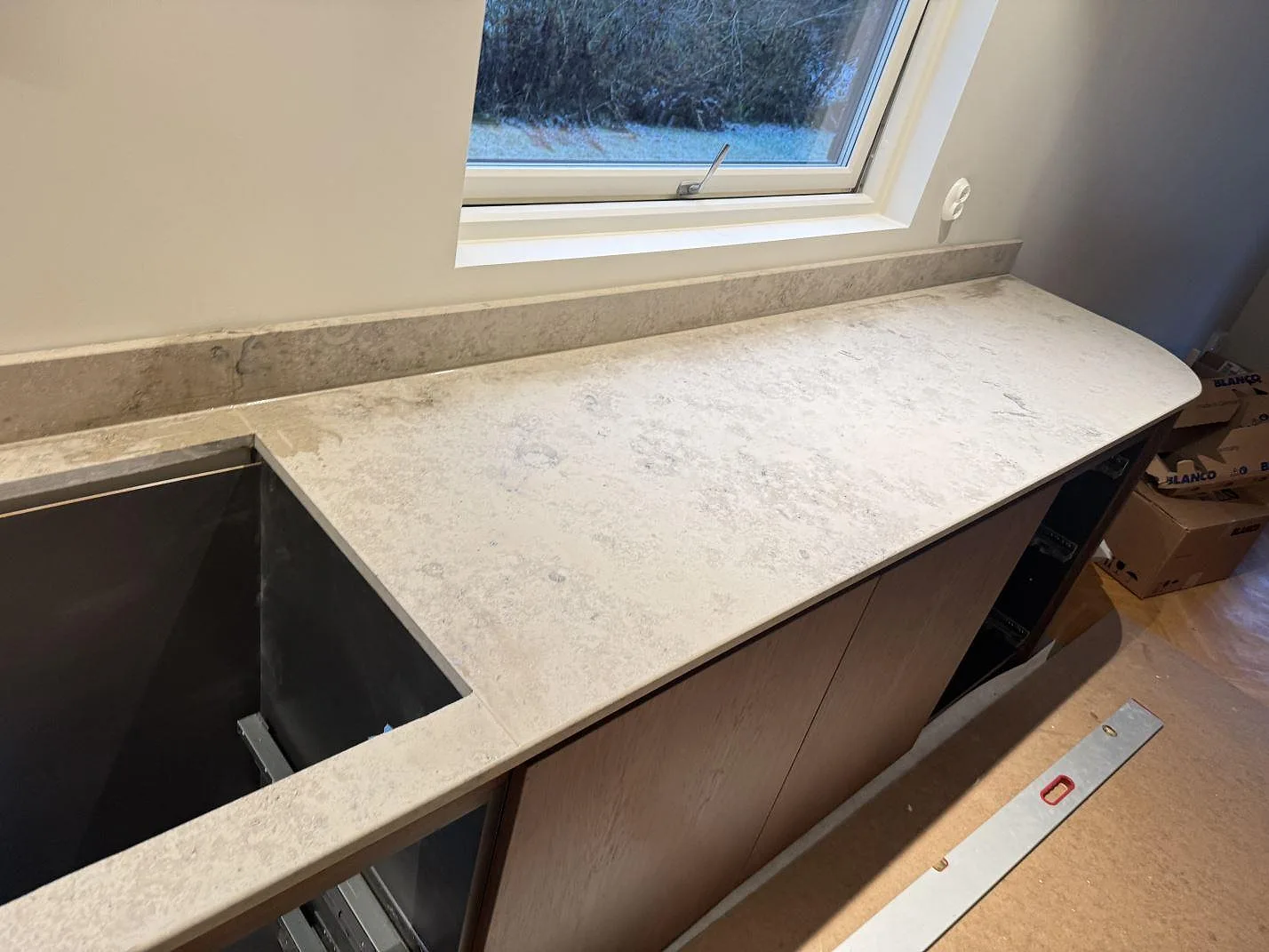 Lång köksbänkskiva i matt Jura Grey med hällurtagning, rundad avslutning och stänkkant under fönster i Borås.