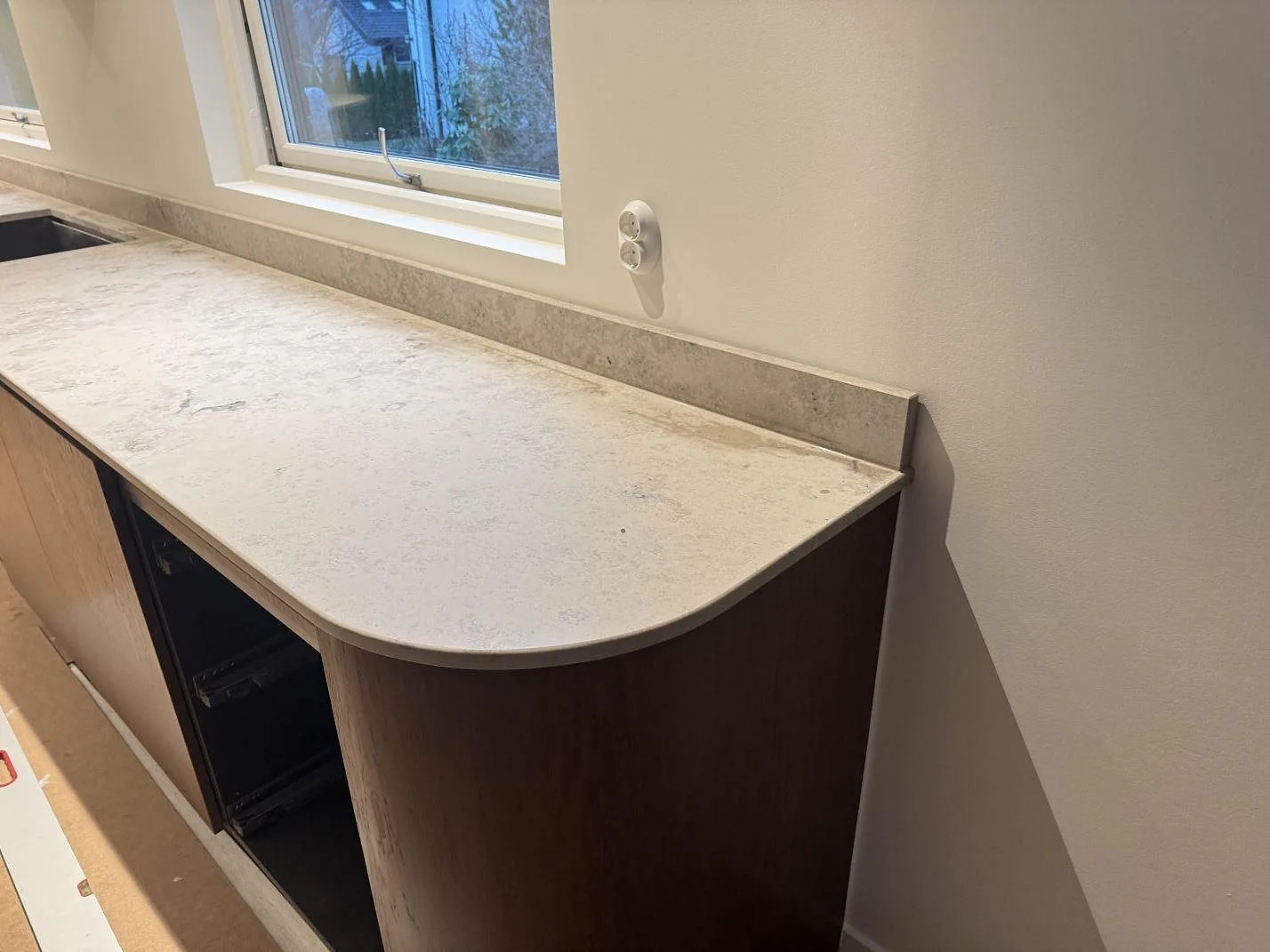 Rundat ändstycke på en matt Jura Grey bänkskiva med låg stänkkant längs väggen i ett kök i Borås.