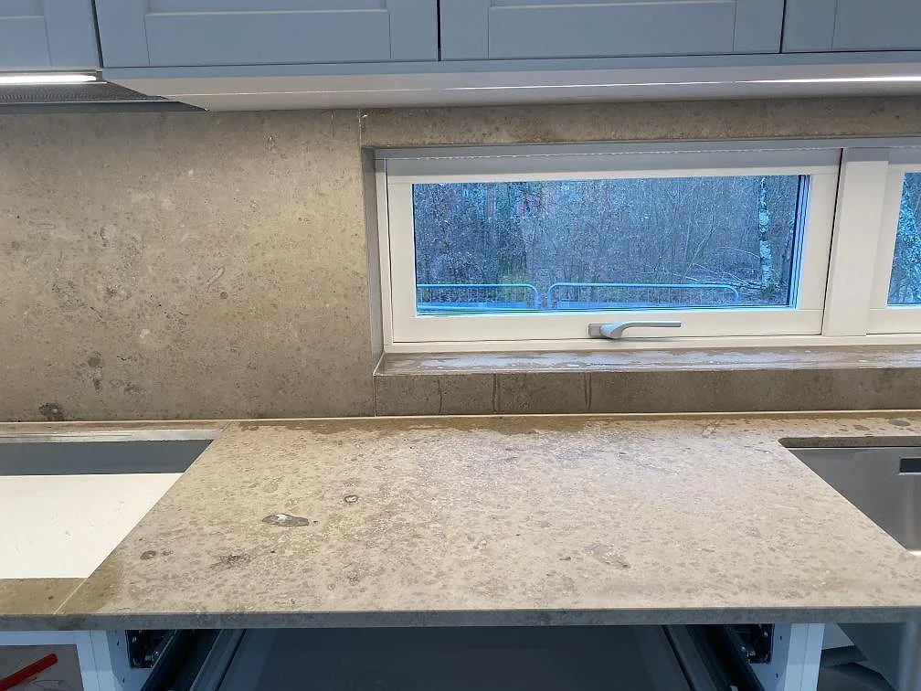 Matt Jura Grey köksbänkskiva med stenfönsterbänk och stänkskydd, fotad mot fönstret under montering i ett kök i Brösarp.