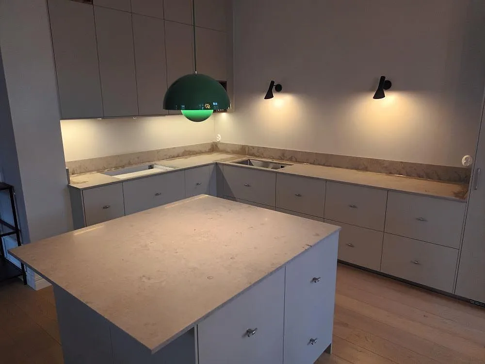 Köksö och L-formad bänkskiva i matt Jura Grey kalksten i ett Bromma-kök, med fossilådring i stenen och underlimmad dubbeldiskho.