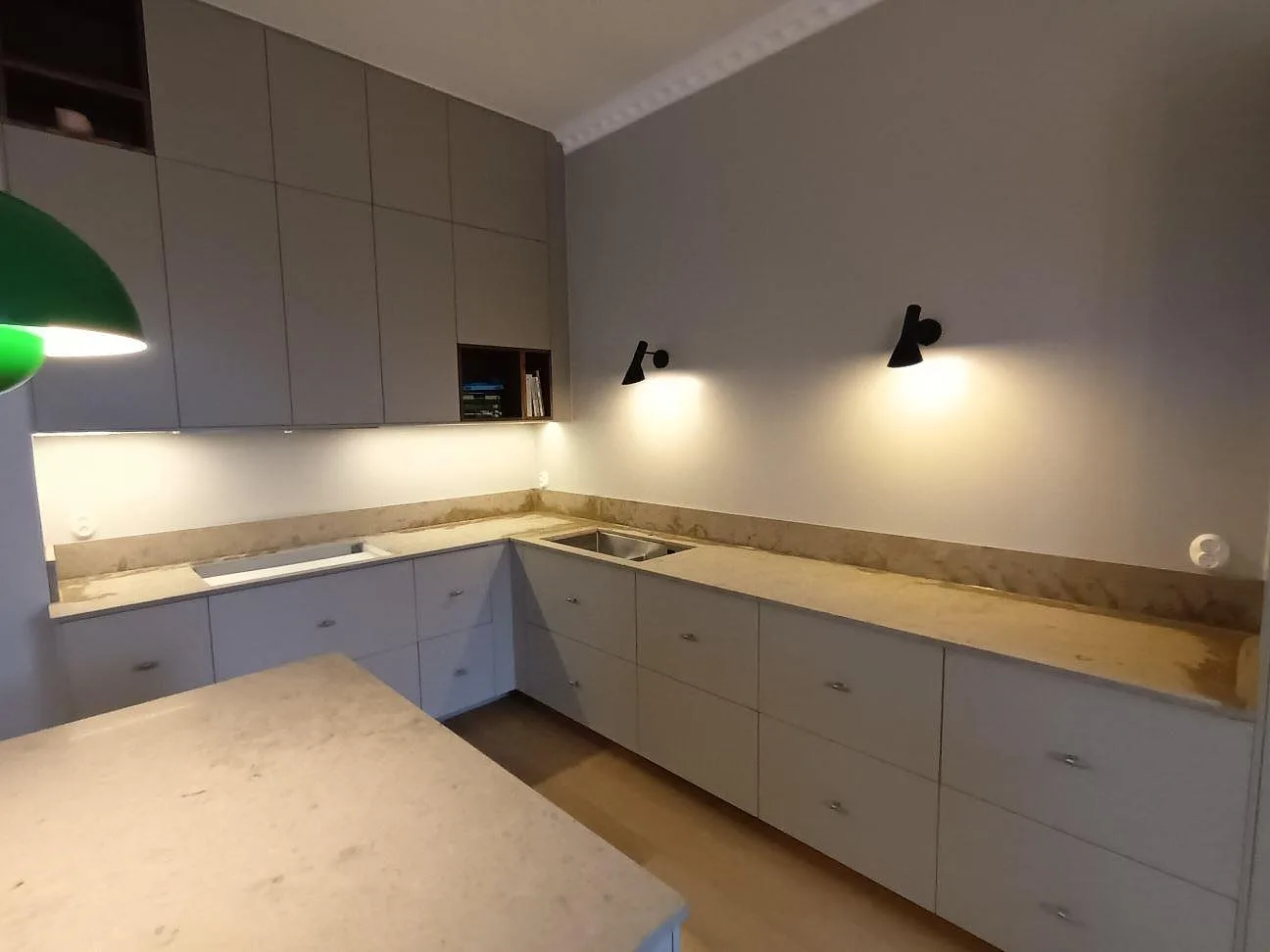 Närbild på den L-formade köksbänkskivan i Jura Grey kalksten i Bromma, med underlimmad diskho, urtag för häll och uppvikt stänkkant.