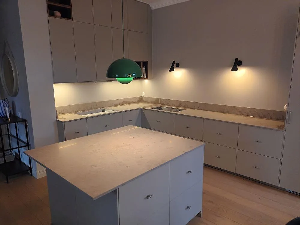 Köksbänkskiva och köksö i Jura Grey kalksten med matt yta i ett kök i Bromma, med ljusgrå luckor, underlimmad diskho och låg stänkkant.
