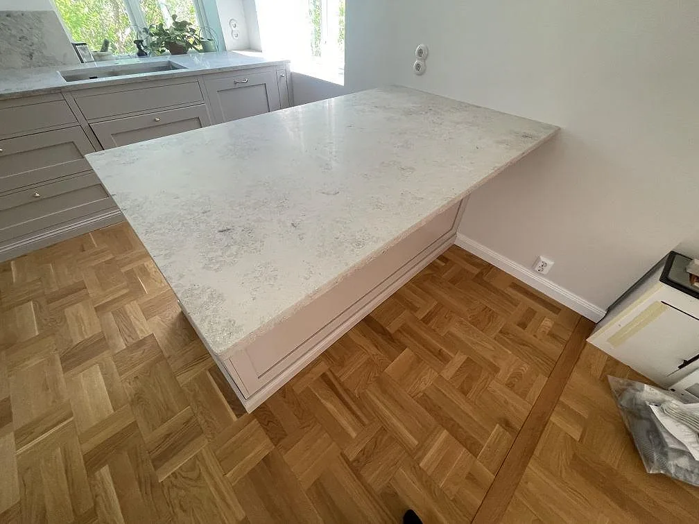 Köksö i matt Jura Grey kalksten med fossilrik gråbeige yta och bänk vid fönster i Bromma.