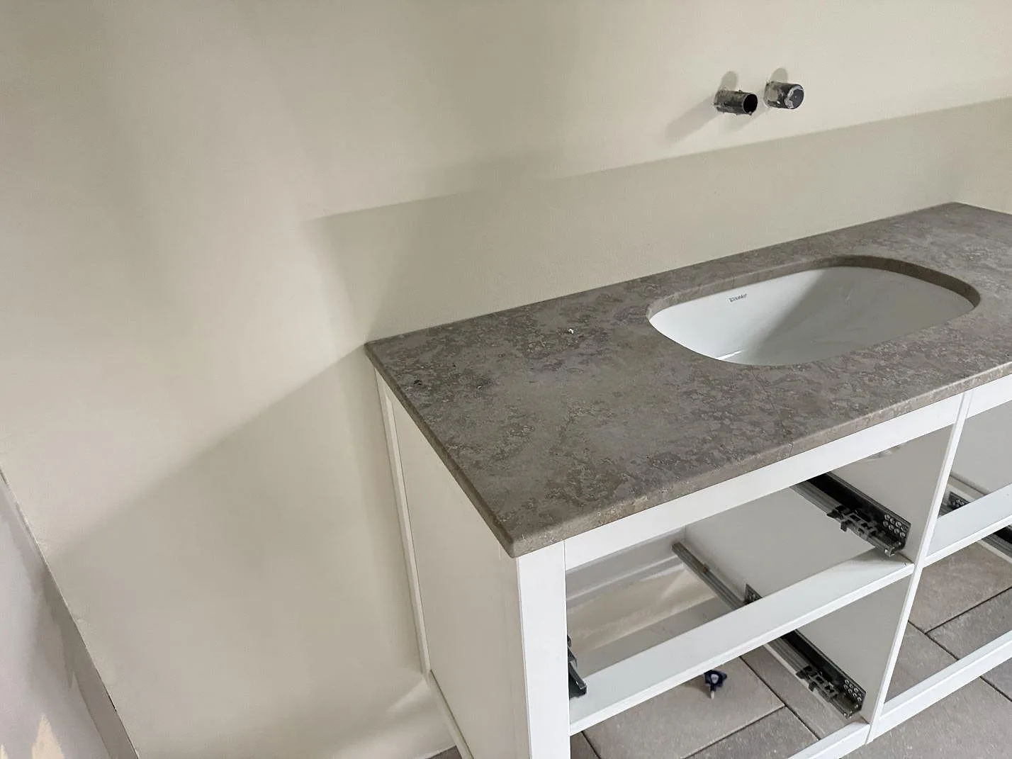 Bänkskiva i matt Jura Grey kalksten med tvättställ och öppna kommodstommar under montering i Espergaerde.