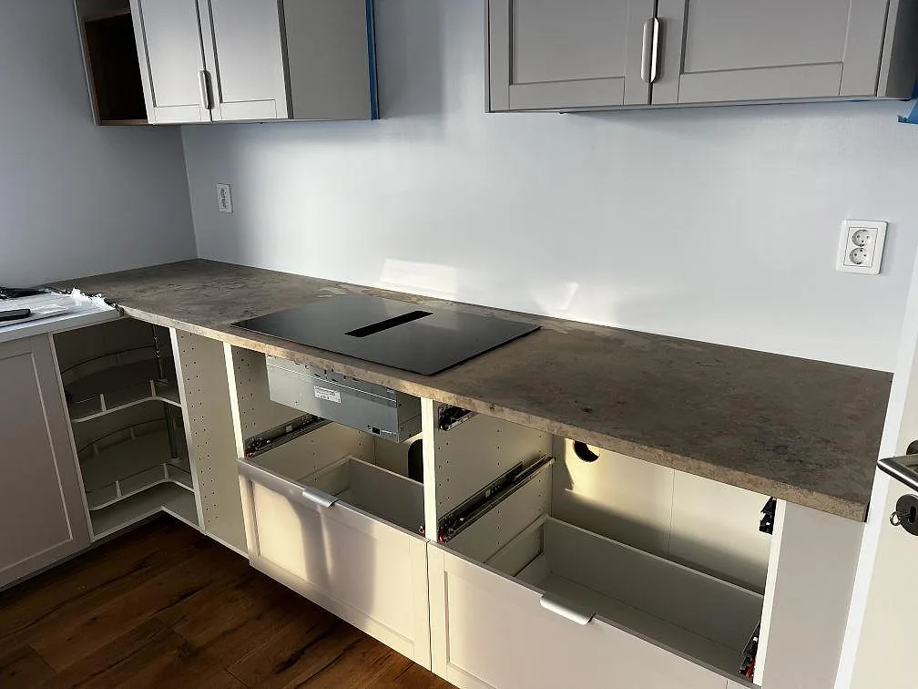 Köksbänkskiva i matt Jura Grey kalksten med svart induktionshäll och vita köksstommar i Falsterbo.
