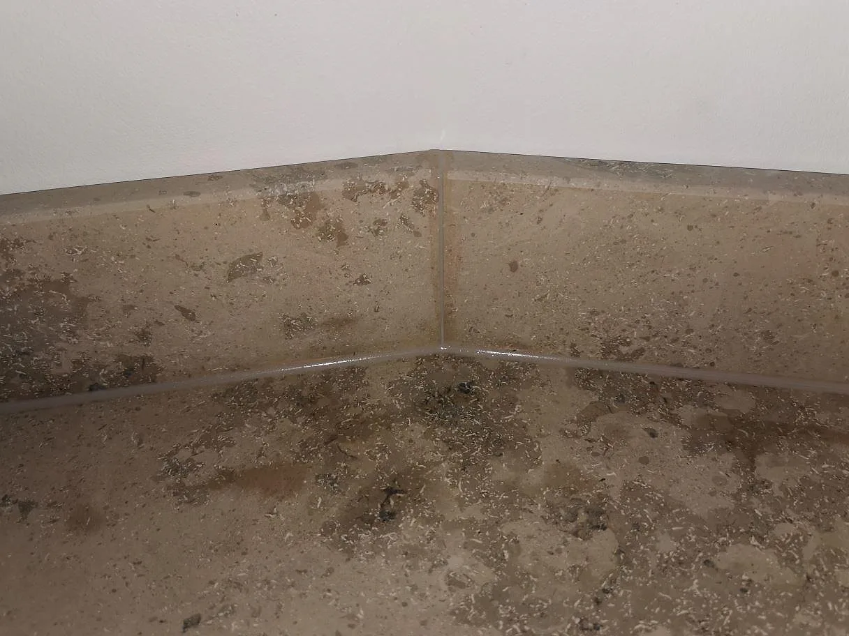 Närbild på den fossilrika ytan i matt Jura Grey kalksten med skarven mellan bänkskiva och uppvikt stänkkant i ett kök i Frederiksberg.