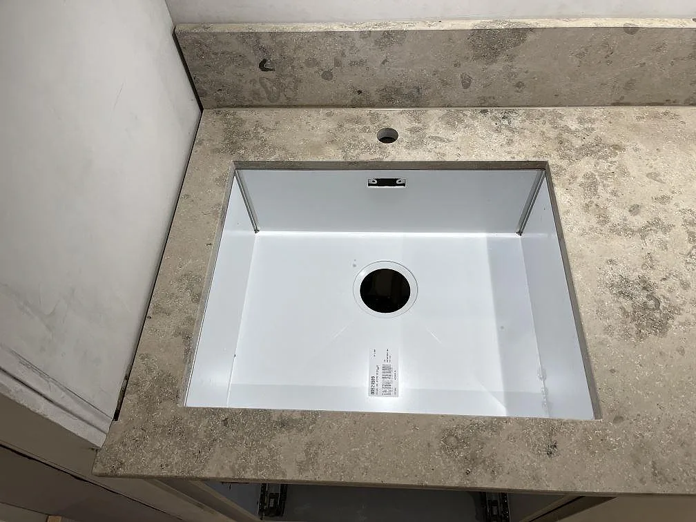 Underlimmad diskho monterad under en Jura Grey bänkskiva i kalksten med separat borrat blandarhål, i ett kök i Göteborg.