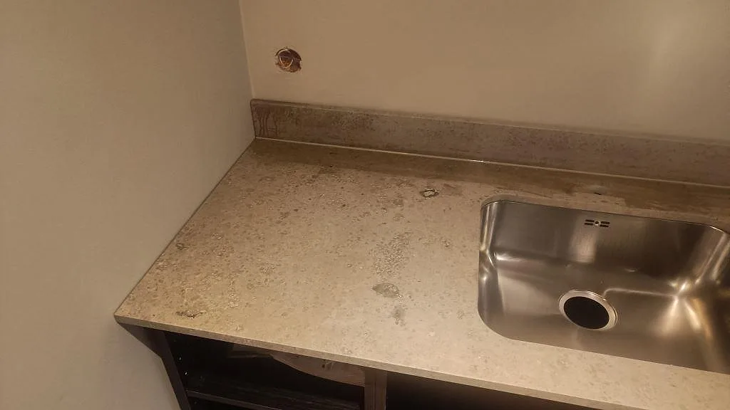 Närbild på matt Jura Grey kalksten med rostfri diskho, stänkkant och öppna köksstommar i Göteborg.