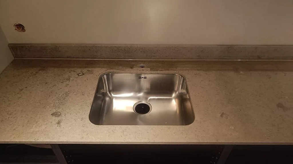 Underlimmad rostfri diskho infälld i matt Jura Grey bänkskiva med synlig fossilådring i ett kök i Göteborg.