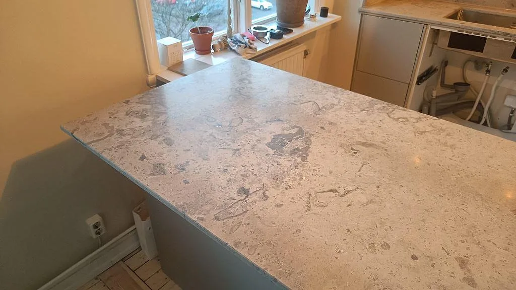 Närbild på halvö i matt Jura Grey kalksten med fossil ådring och ljus från fönster i ett kök i Göteborg.