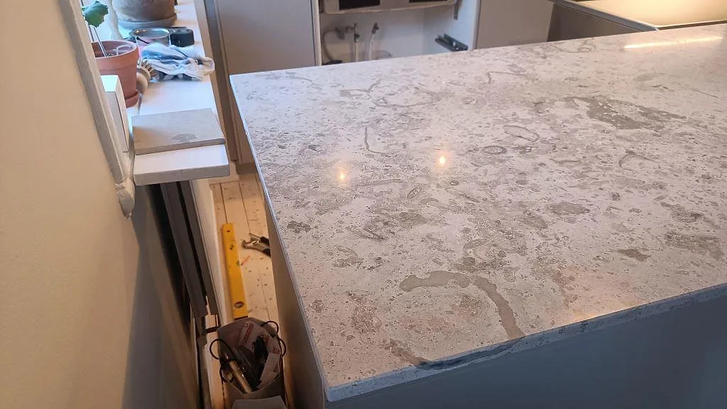 Detalj av kant och yta på halvö i matt Jura Grey kalksten under montering i ett Göteborgskök.