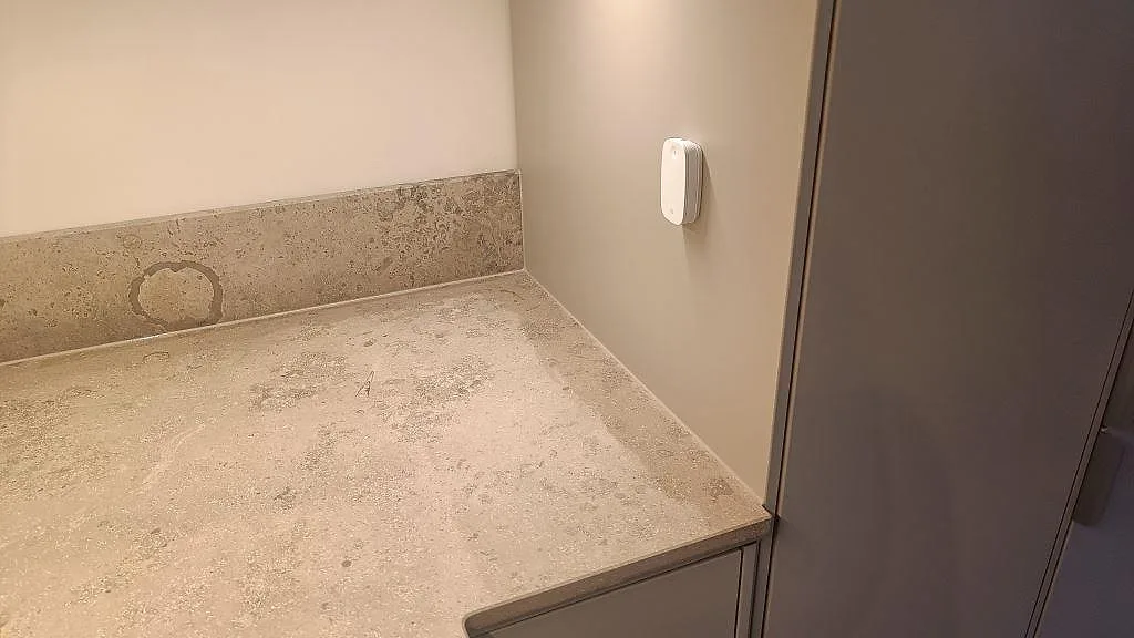 Köksbänkskiva i matt Jura Grey kalksten med uppvikt stänkkant intill mörka luckor i Göteborg.