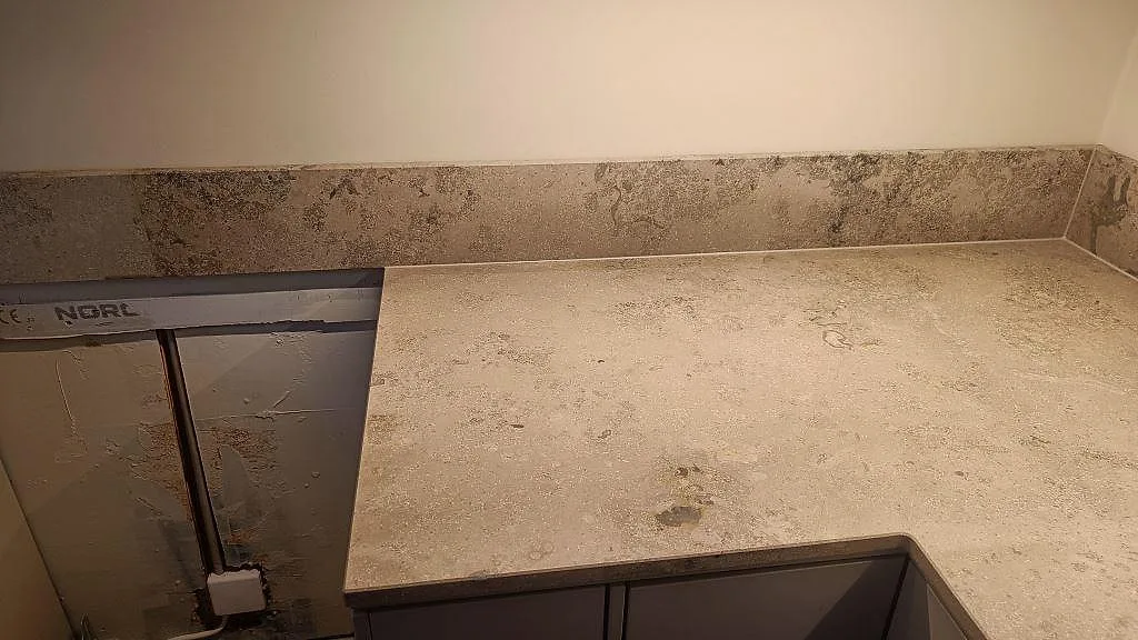 Köksbänkskiva i matt Jura Grey kalksten med stänkkant och mörk köksinredning under montering i Göteborg.